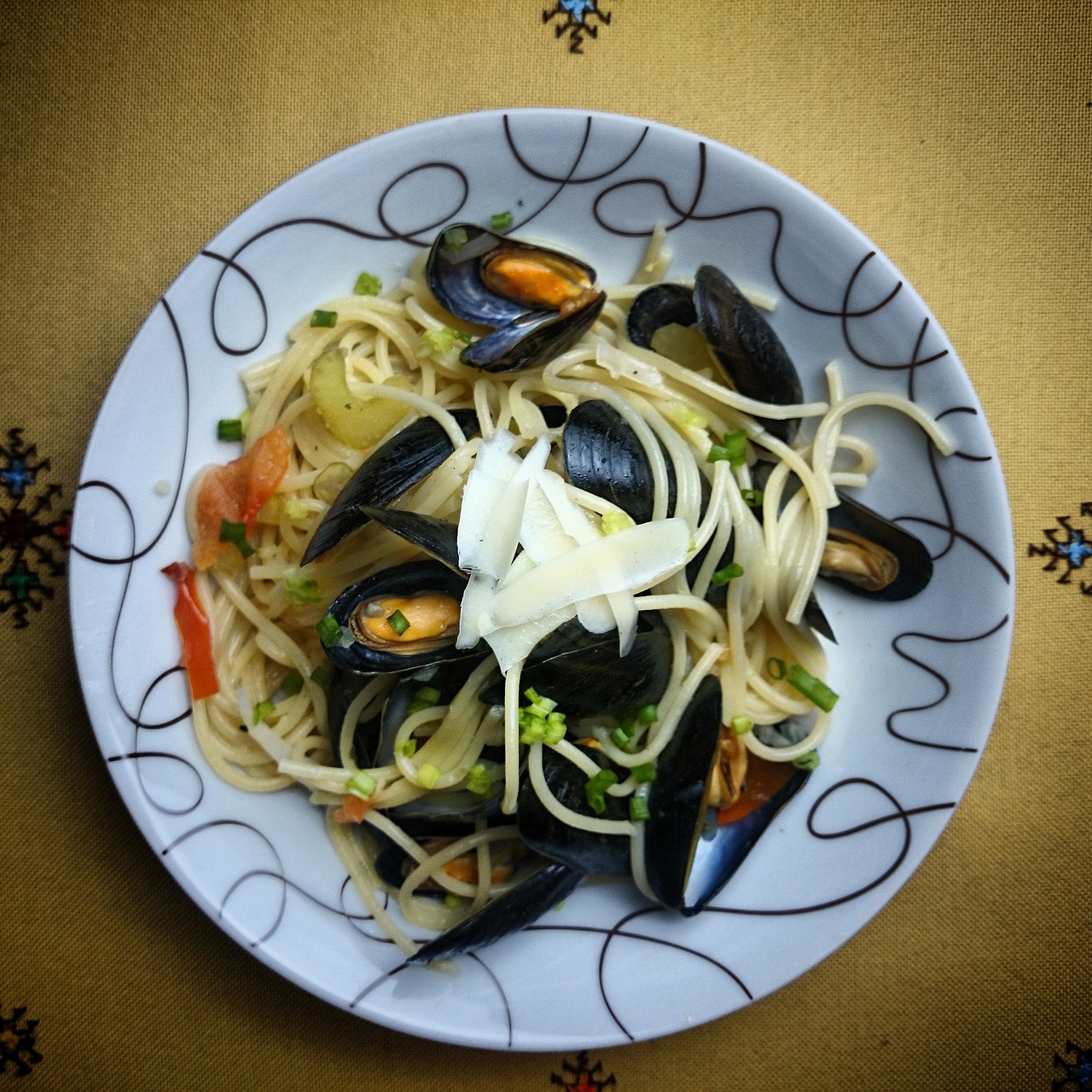 Piatto di pasta con cozze e pecorino, decorato con erbe fresche e un tocco di pepe.